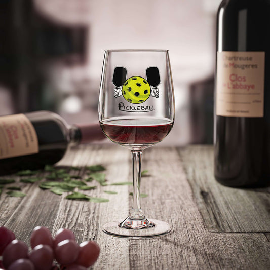 HarmonyGrip Pickleball Series Wine Glass on a rustic table with red wine and bottles in the background.