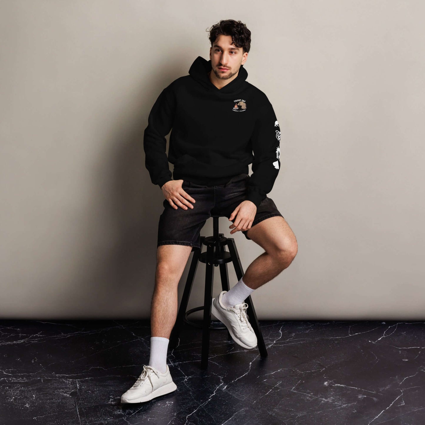 Man sitting on a stool wearing a black oversized hoodie and shorts, ideal for camping or casual outings.