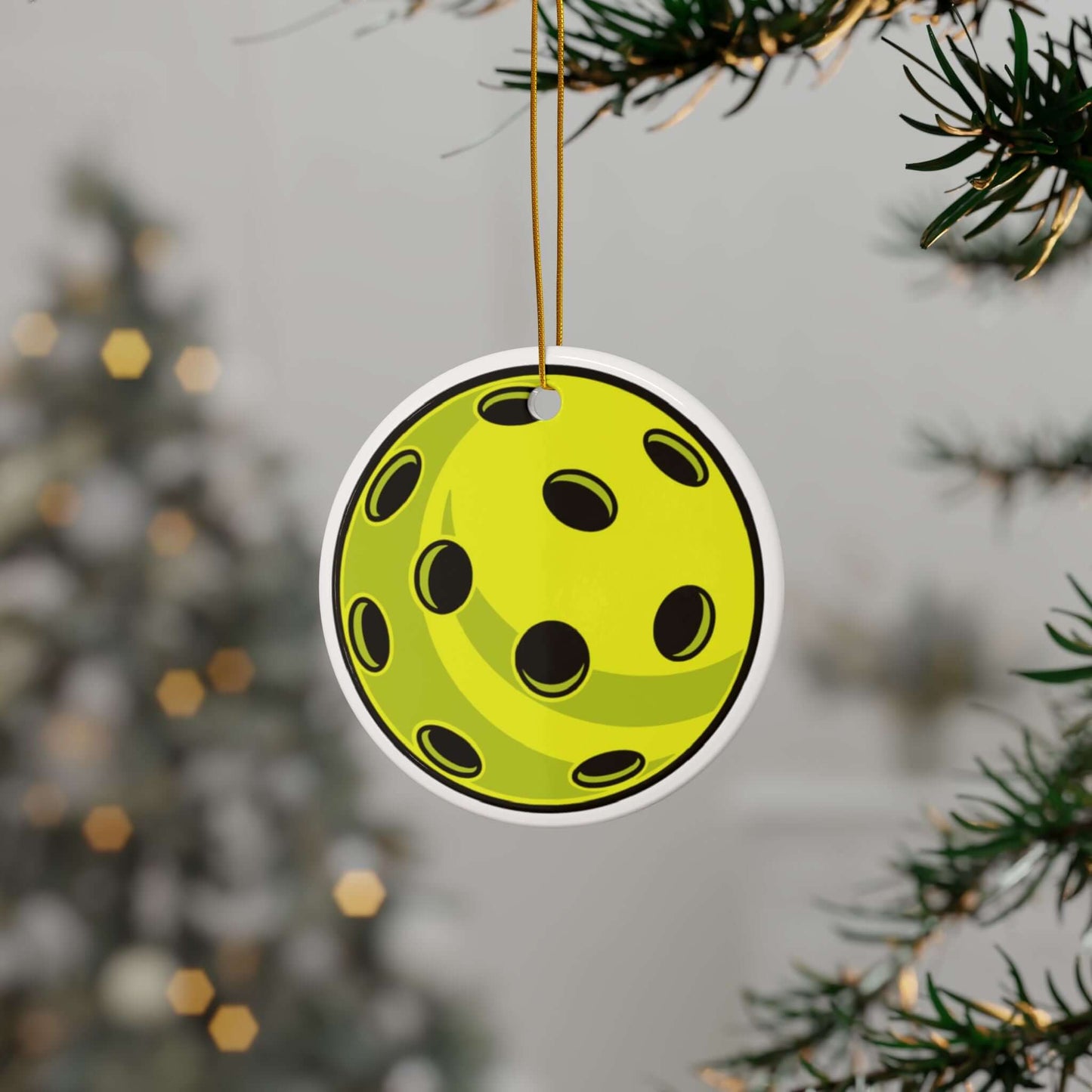 Pickleball-themed ceramic Christmas ornament hanging on a tree, featuring a vibrant two-sided print with a holiday background.