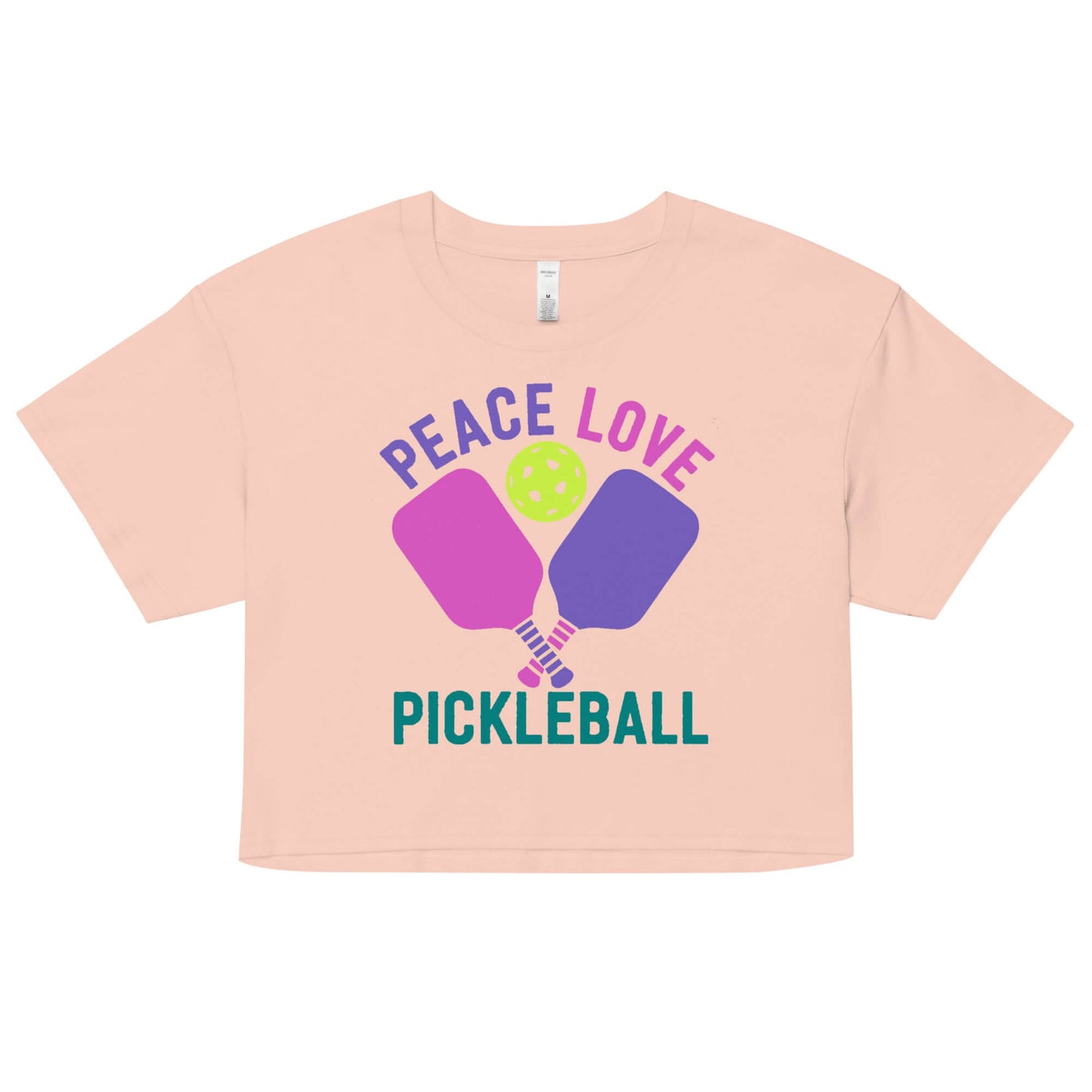 Women’s Peace, Love, Pickleball Crop Top with vibrant design and pickleball paddles in soft peach color.