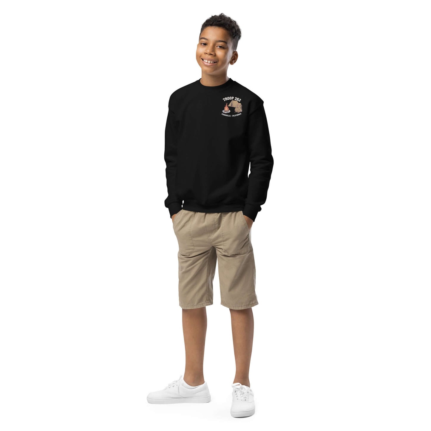 Smiling boy wearing a black Youth Crewneck Sweatshirt with camping design and khaki shorts.