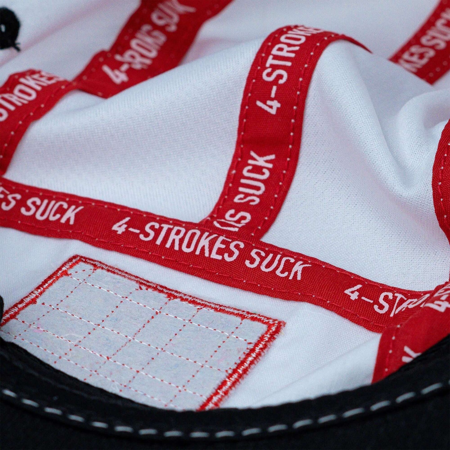 Close-up of the inside of a hat featuring red bands with "4-STROKES SUCK" text, white fabric, and a stitched patch.