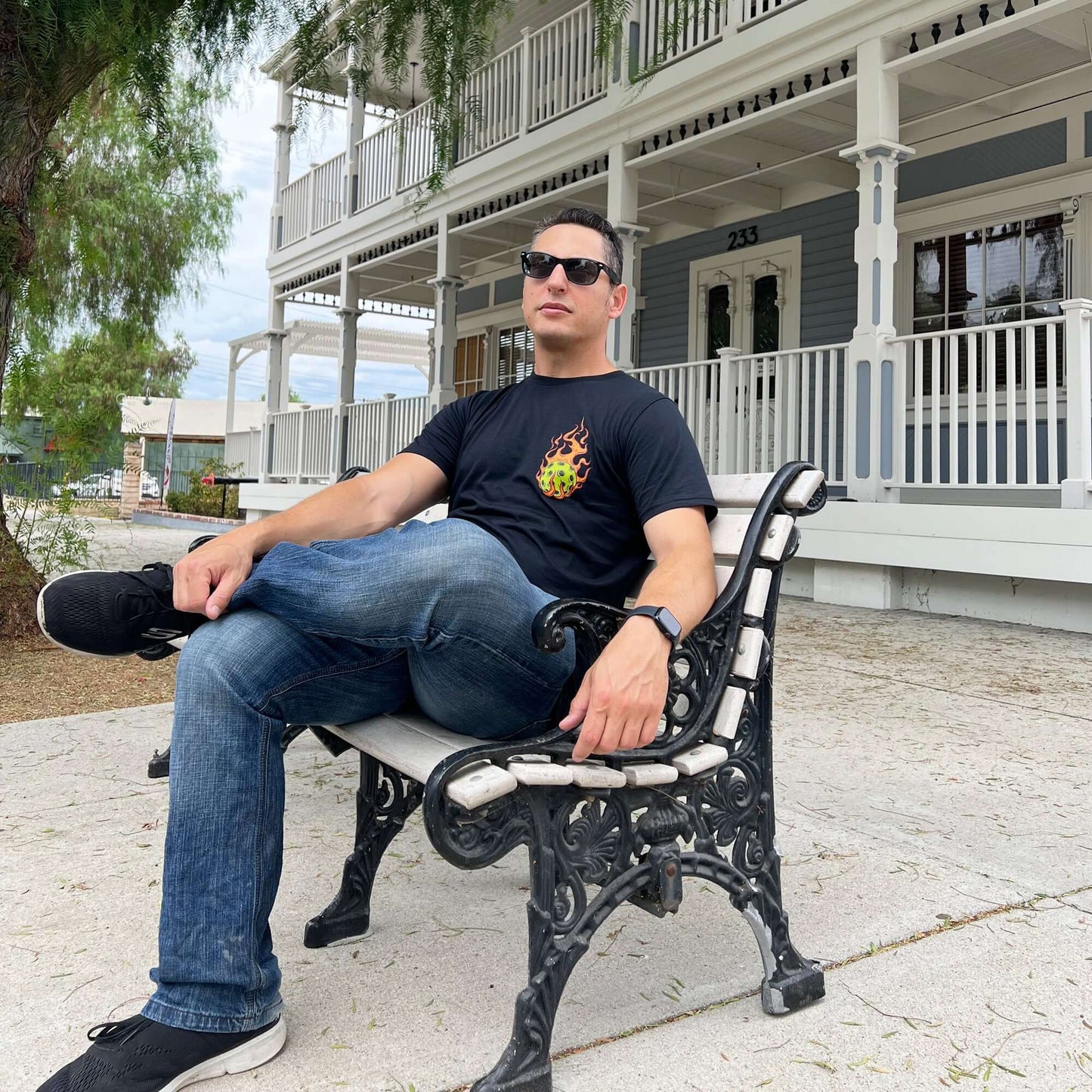 Man wearing flaming pickleball black t-shirt sitting on bench, intimidating design symbolizing power and skill in pickleball.
