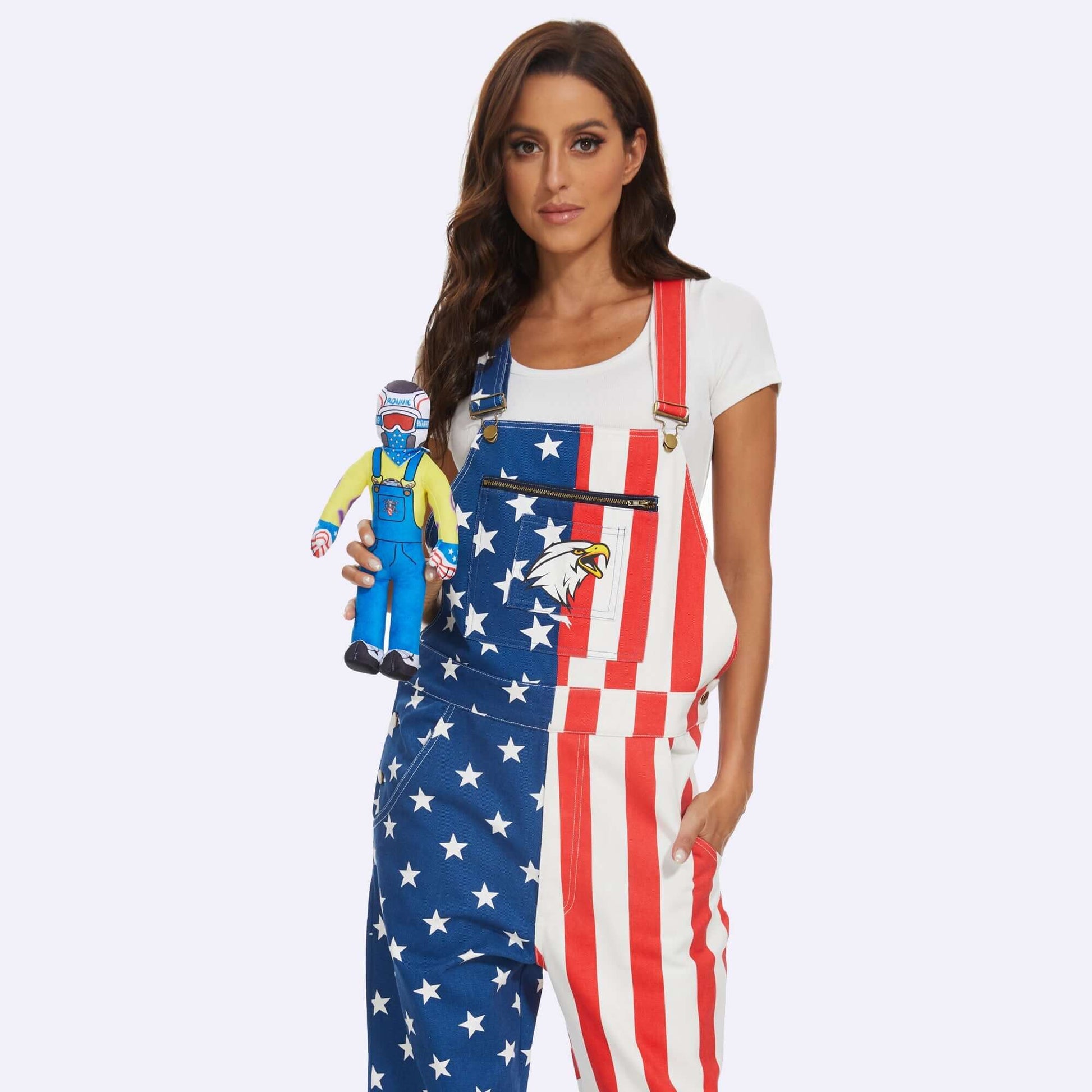 Woman holding Lil Ronnie Plush, wearing American flag overalls, on a plain background.