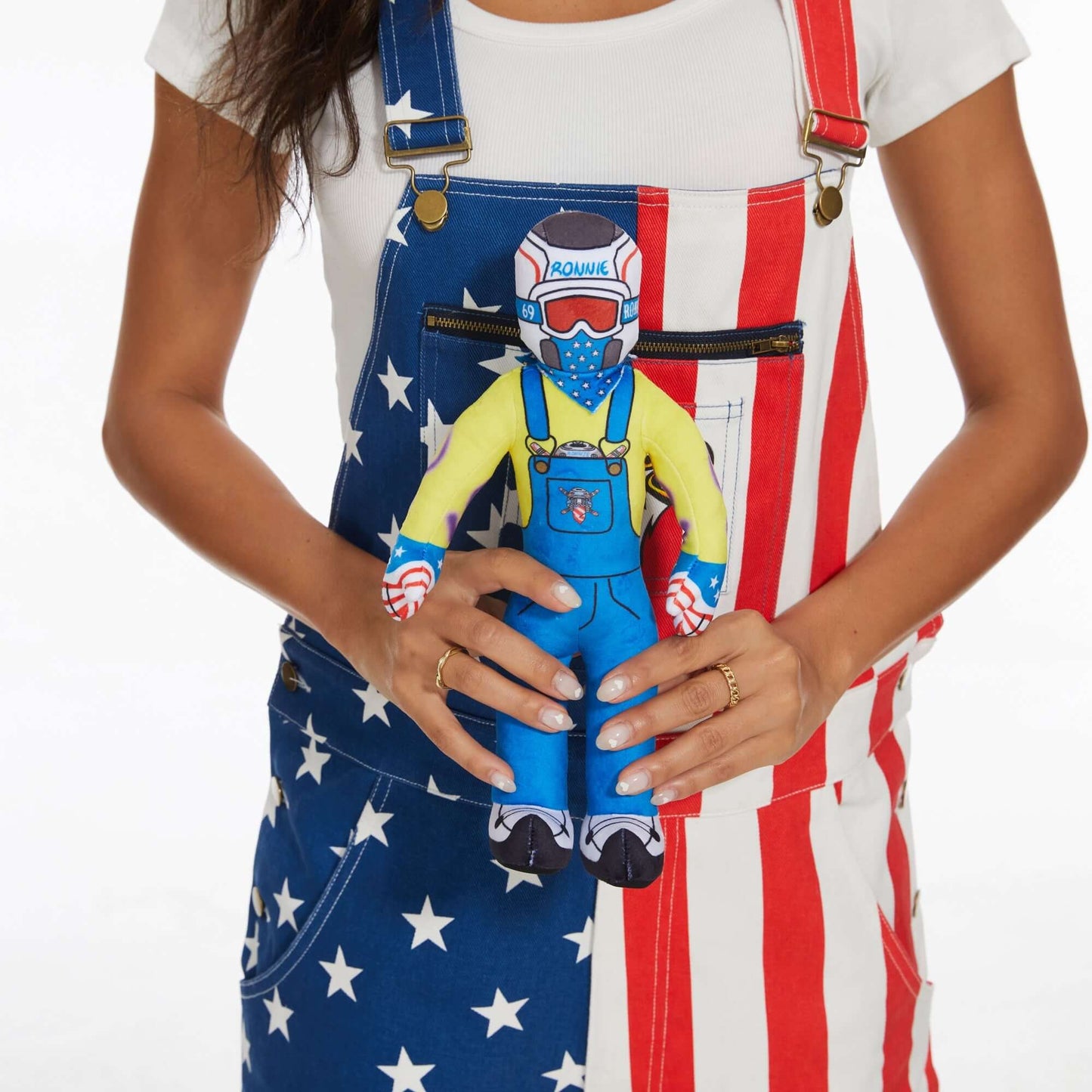 Woman holding Lil Ronnie Plush doll in colorful overalls with stars and stripes.