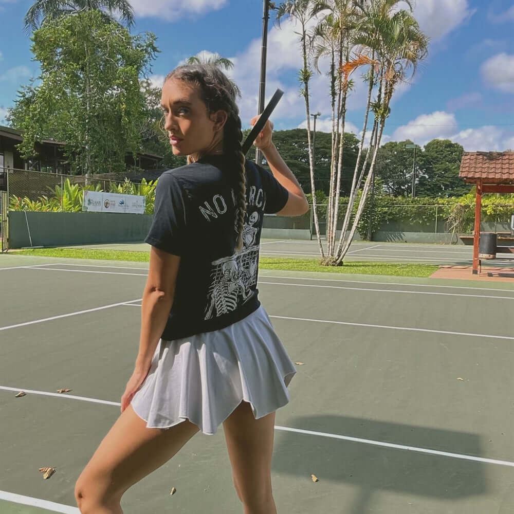 Woman wearing a No Mercy Pickleball black T-shirt on a tennis court, showcasing its bold design and sporty style.