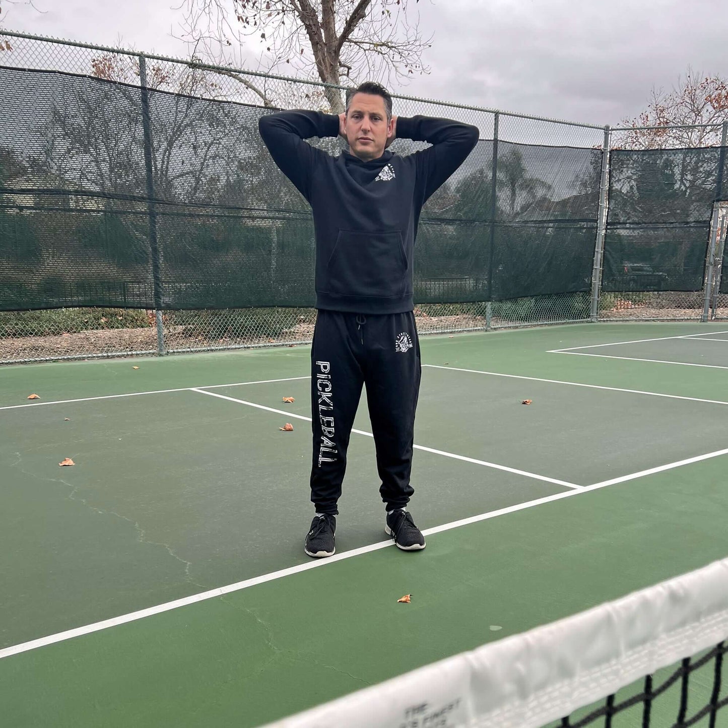 Person wearing black pickleball joggers and sweatshirt standing on a court, highlighting RND Streetwear's comfy sportswear.