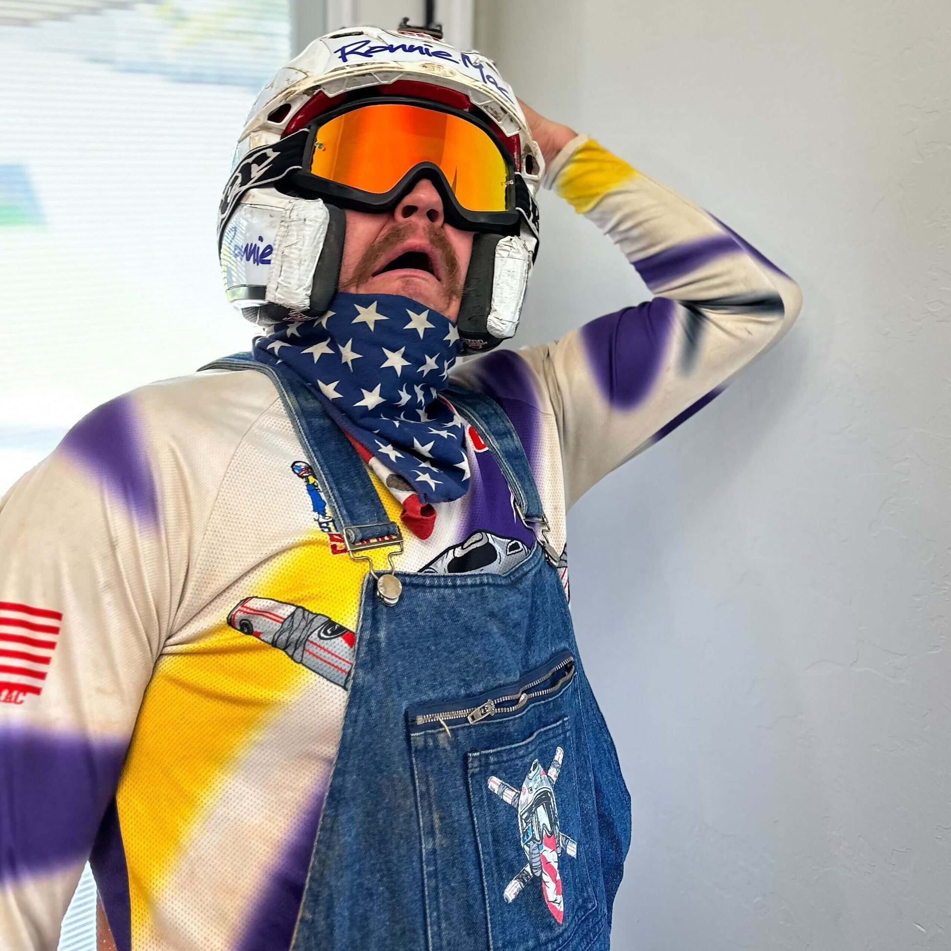 Person wearing goggles and a helmet with an expression of surprise, dressed in a colorful outfit and denim overalls.