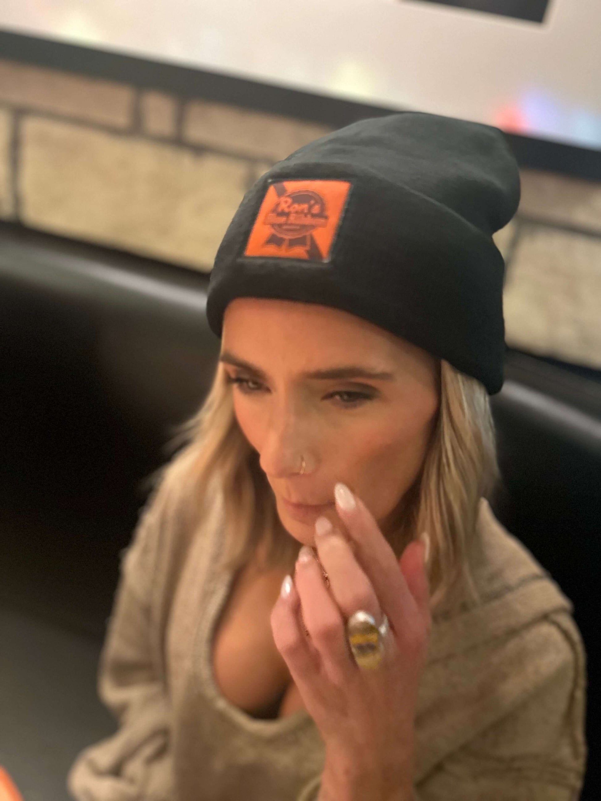 Stylish woman wearing a Ron's Blue Ribbon Beer black beanie indoors.