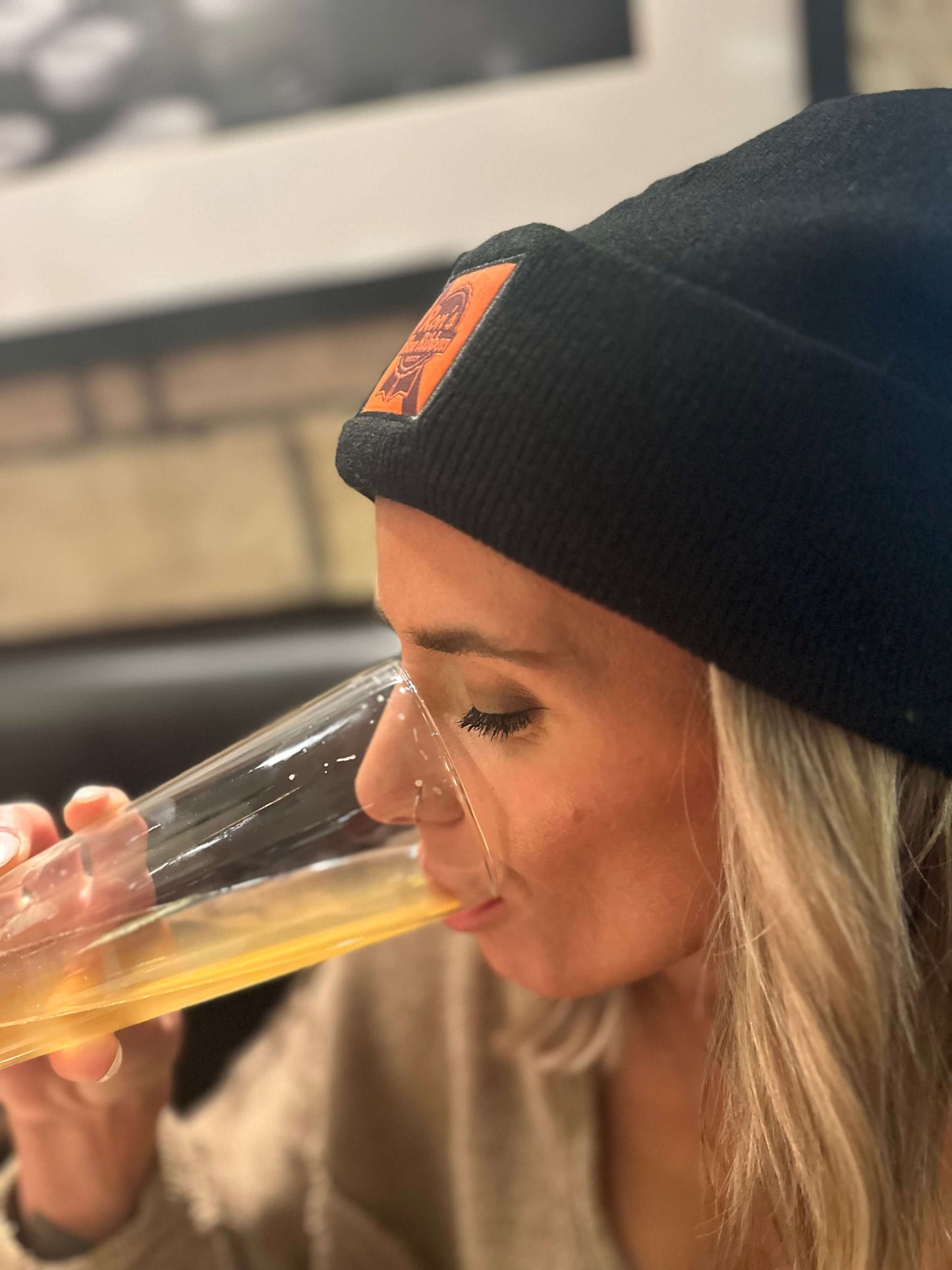 Woman wearing Ron's Blue Ribbon Beer black beanie enjoying a drink.