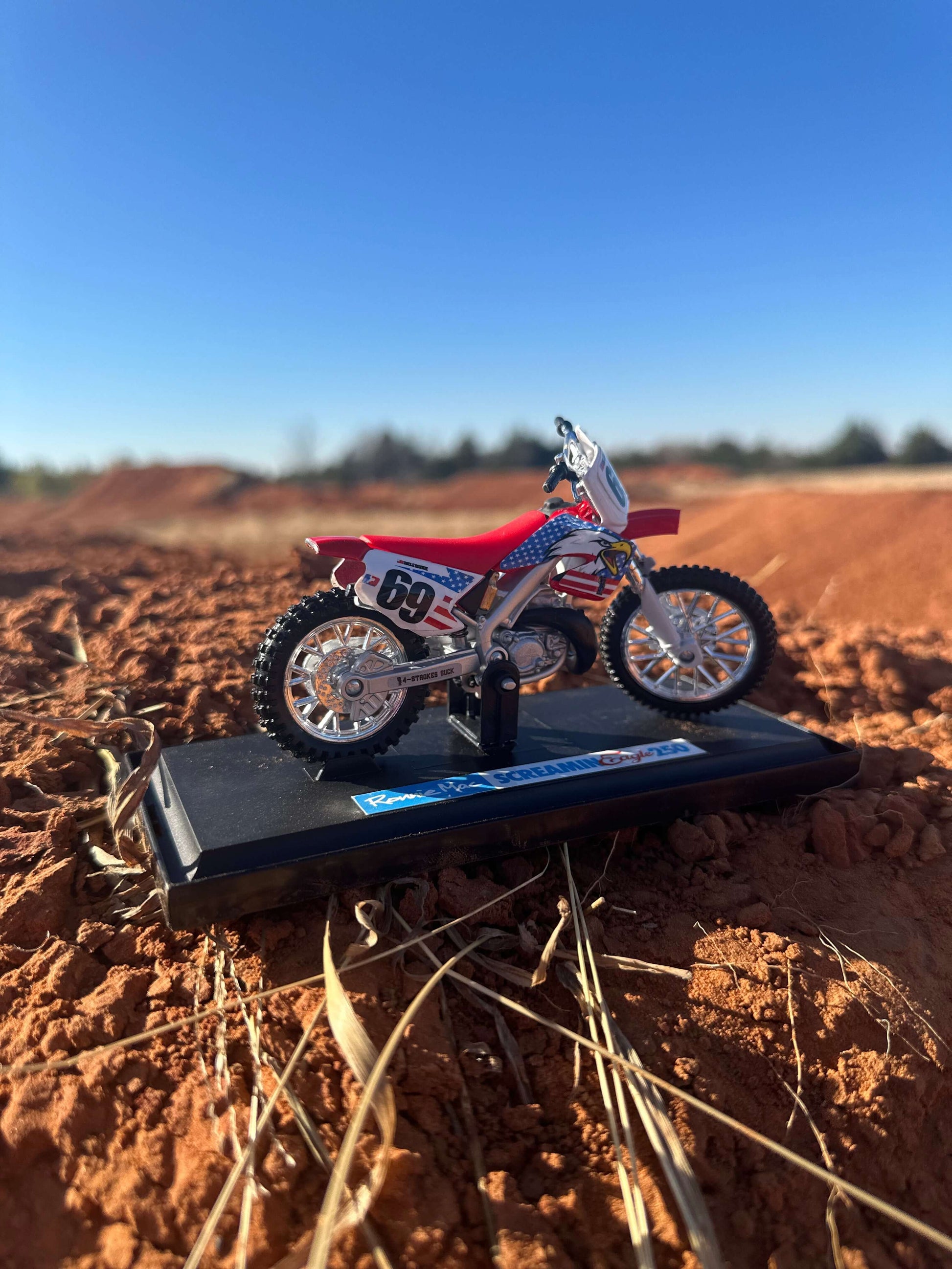Screamin Eagle 250 Replica Dirt Bike Collectible on a dirt track background under clear blue sky.