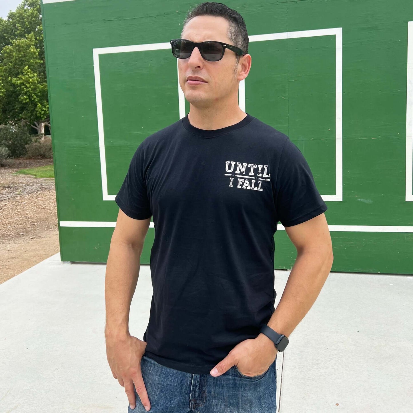Man wearing black "Until I Fall" pickleball t-shirt outdoors, showcasing sporty and determined style.