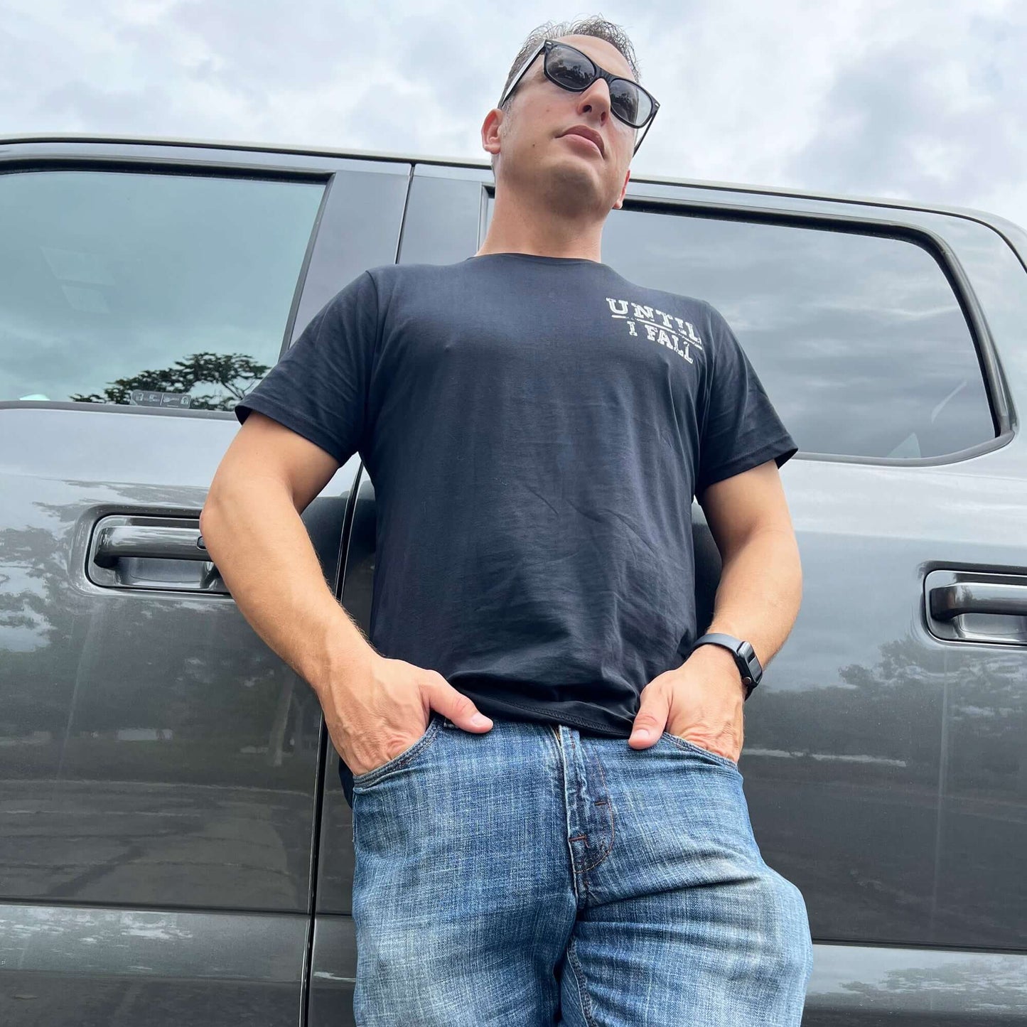 Man wearing "Until I Fall" pickleball black T-shirt stands confidently by a truck.