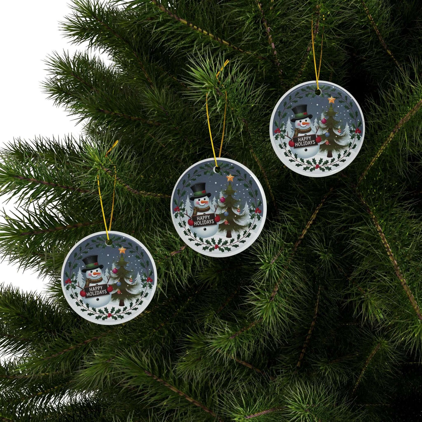 Festive two-sided ceramic ornaments featuring jolly snowman and Christmas tree hang on a lush green tree branch.