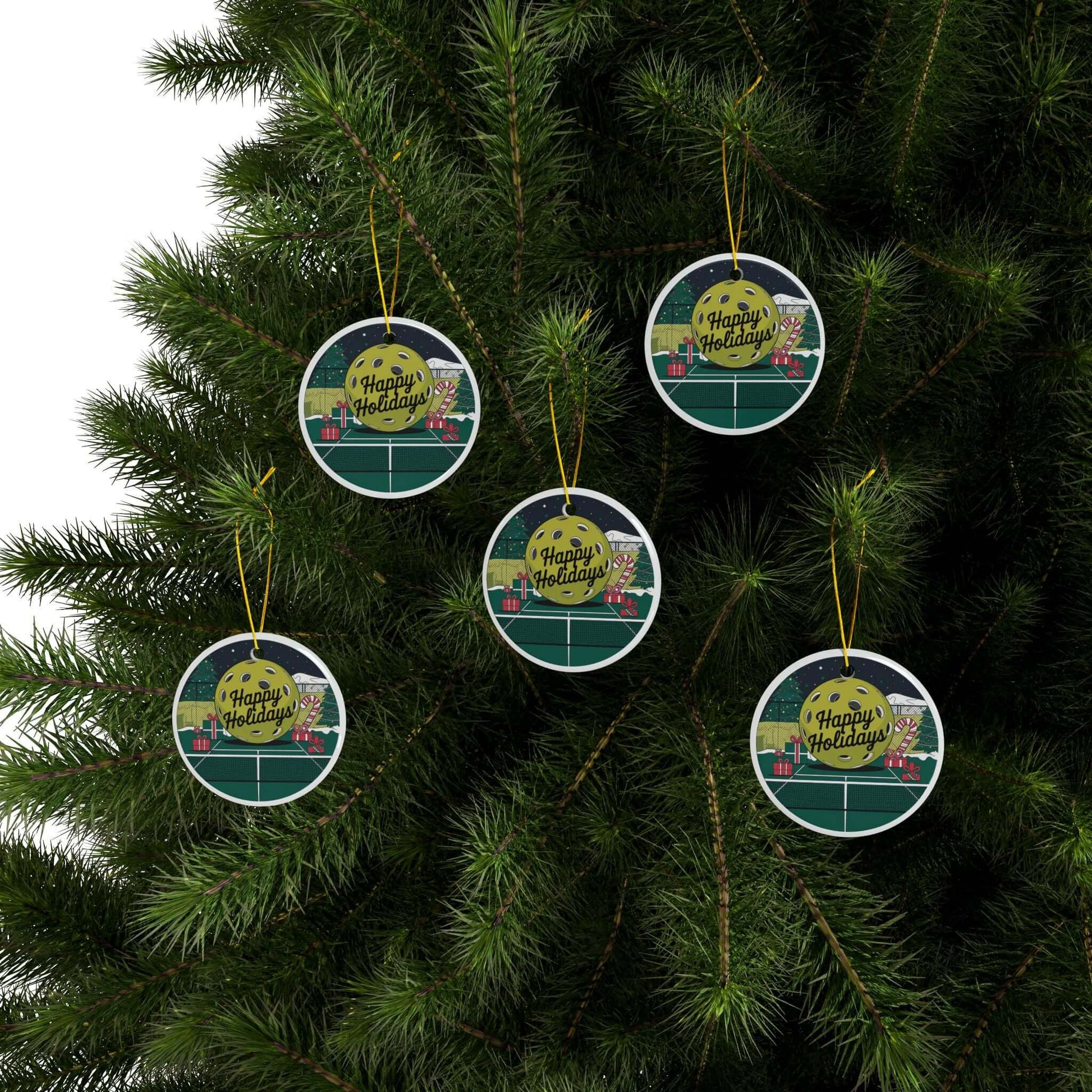 Pickleball-themed ceramic ornaments with "Happy Holidays" text hanging on a Christmas tree, perfect festive décor for enthusiasts.