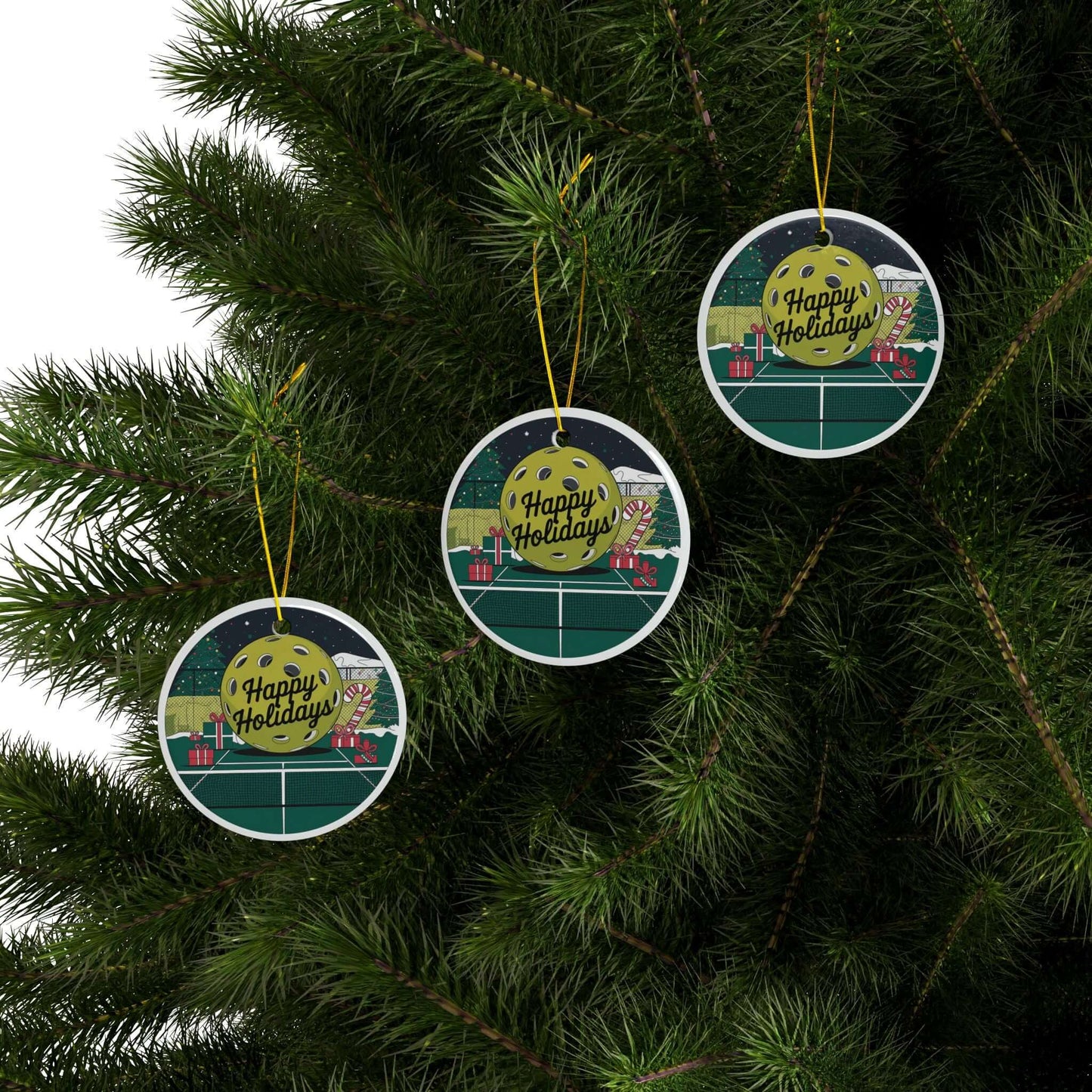 Pickleball holiday court ceramic ornaments hanging on Christmas tree, featuring festive design with "Happy Holidays" text.