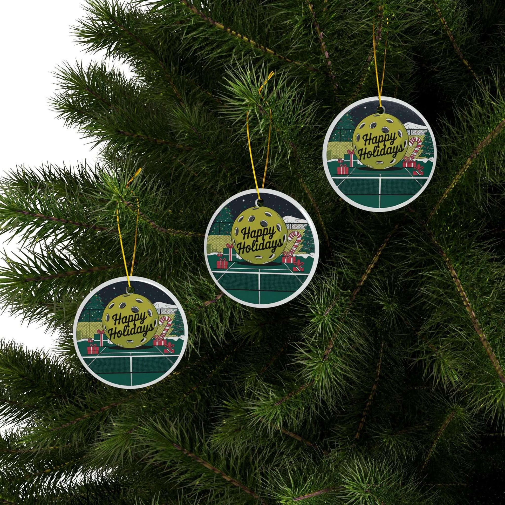 Pickleball holiday court ceramic ornaments hanging on Christmas tree, featuring festive design with "Happy Holidays" text.