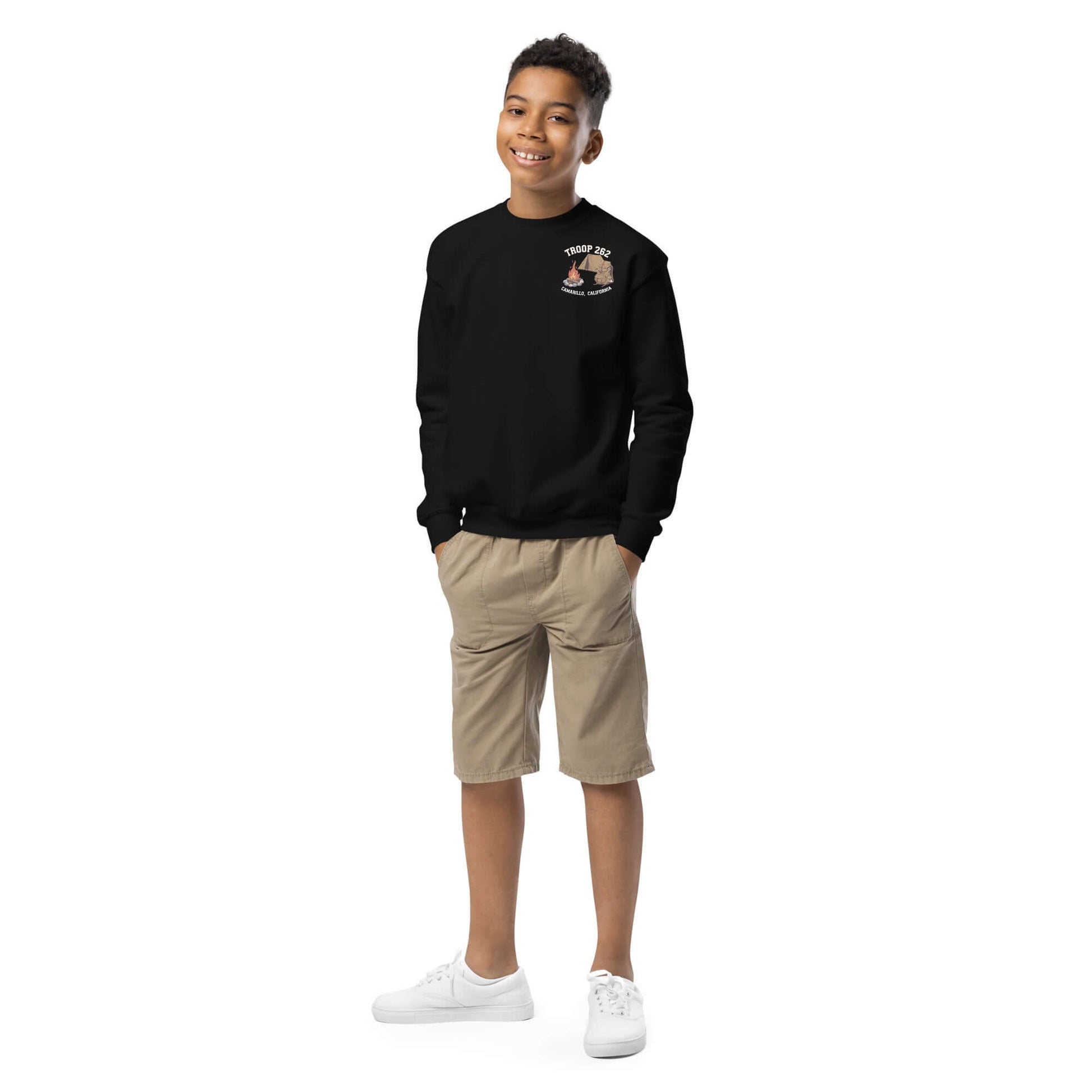 Smiling boy wearing a black Youth Crewneck Sweatshirt with camping design and khaki shorts.