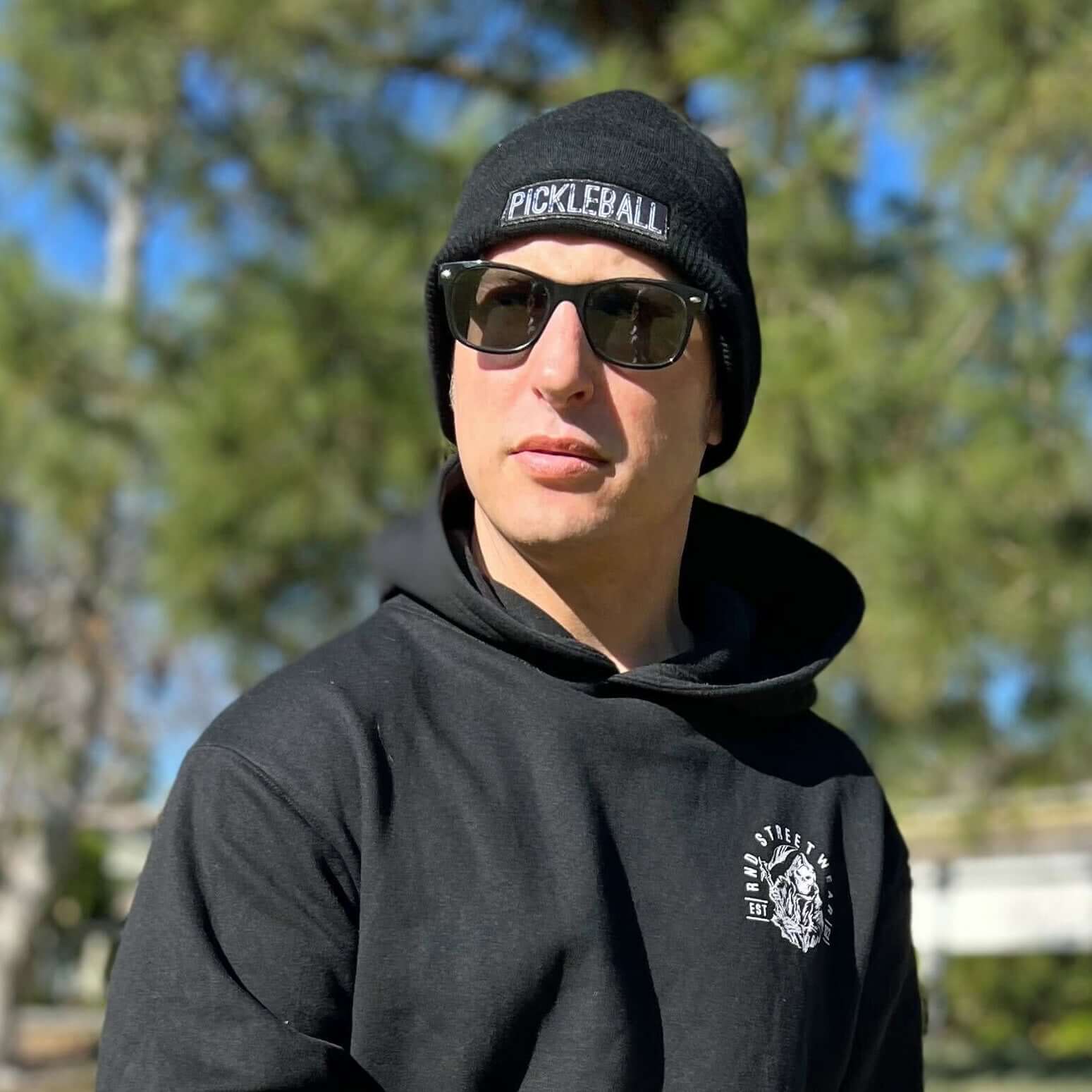 Person wearing black Pickleball Beanie and sunglasses outdoors.