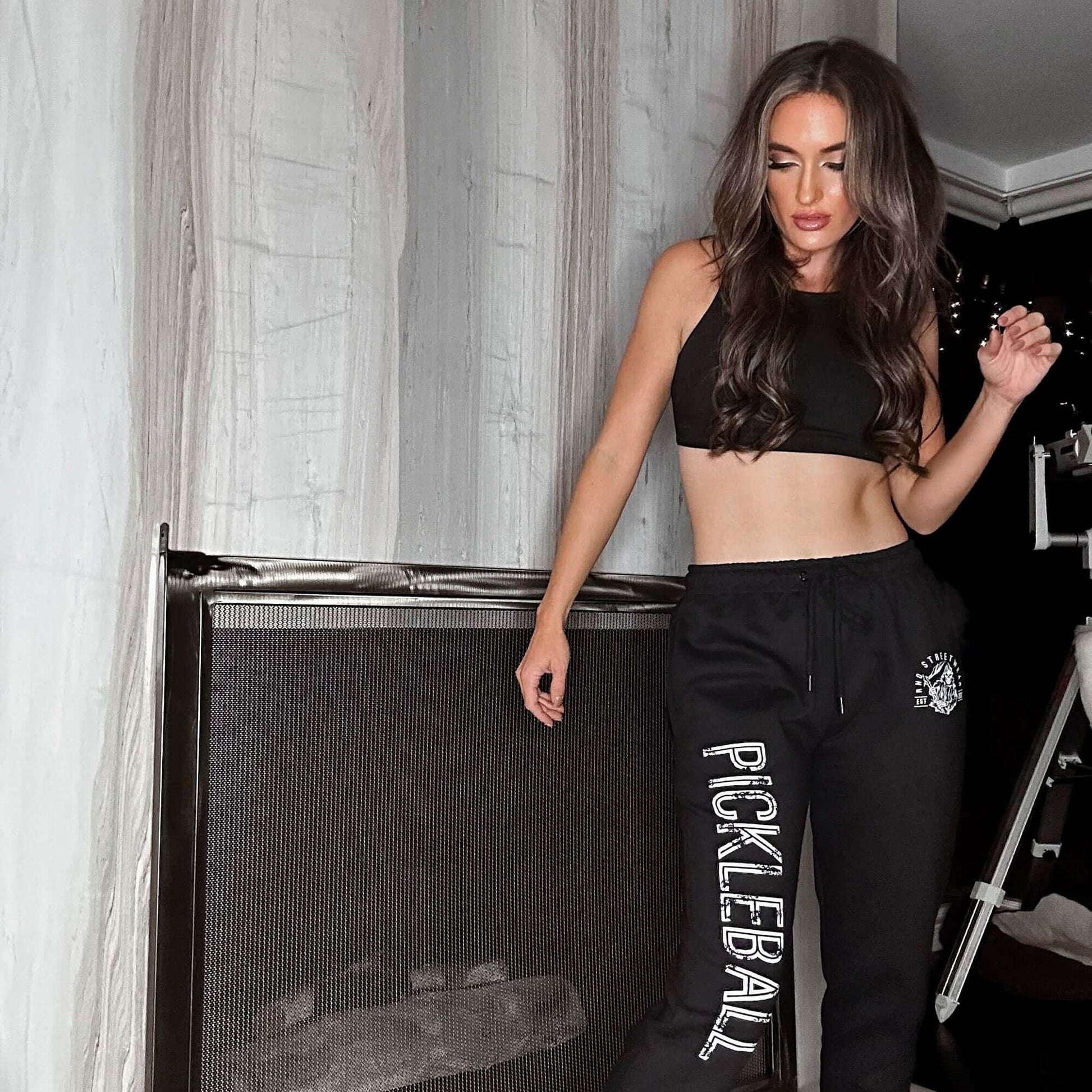 Woman wearing Pickleball black joggers and crop top, showcasing RND Streetwear collection in a modern interior setting.