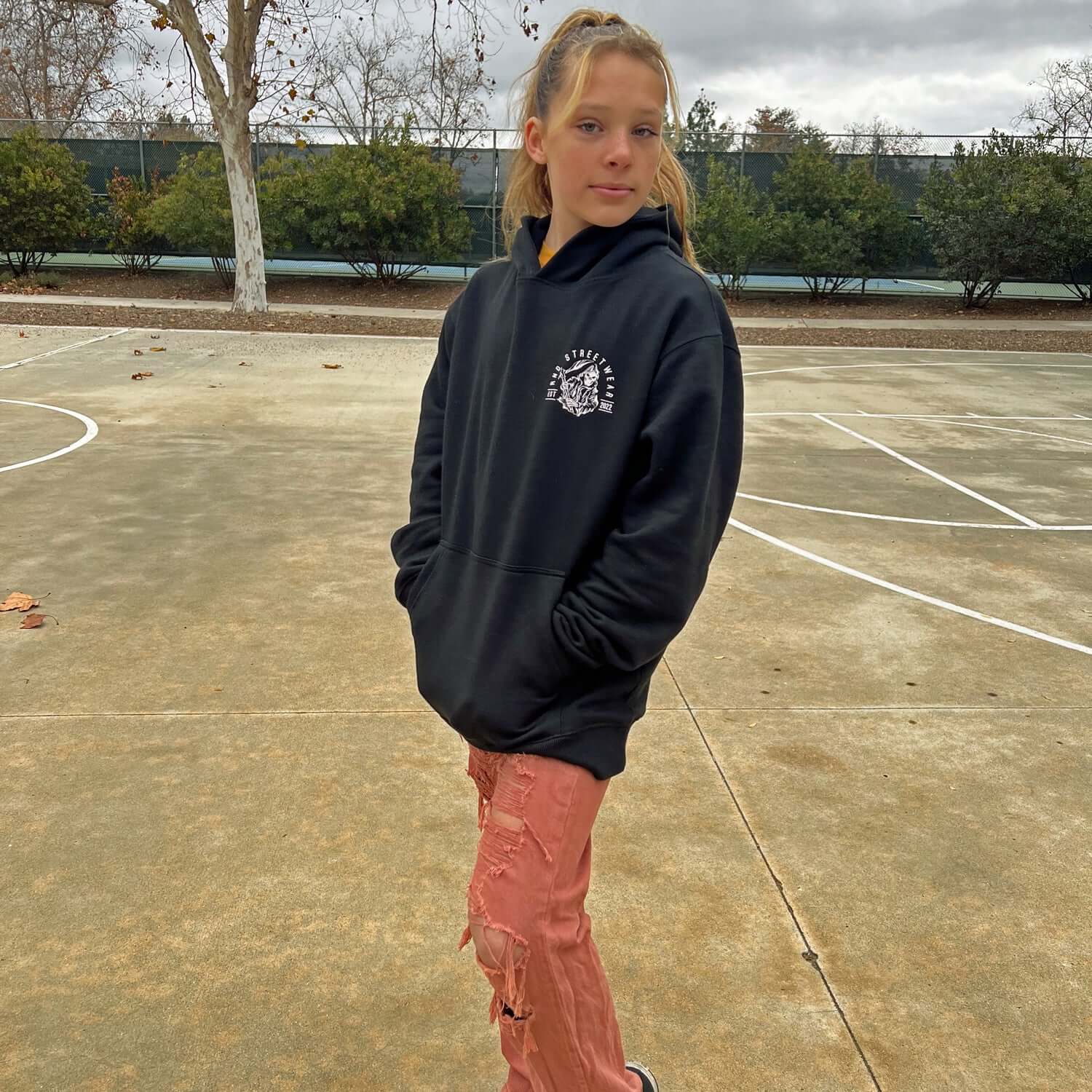 Person wearing black pickleball hoodie with flaming reaper design on empty court.